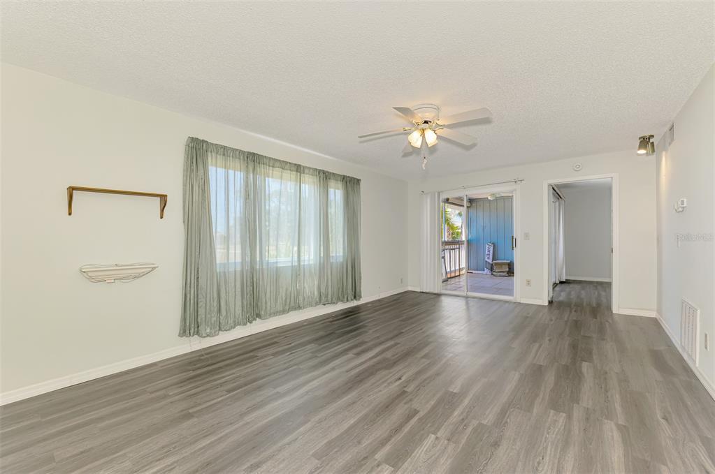 A living room features light-colored walls, gray wood-look flooring, a ceiling fan, and sliding glass doors — 200 ROTONDA BOULEVARD W UNIT A2, ROTONDA WEST, FL