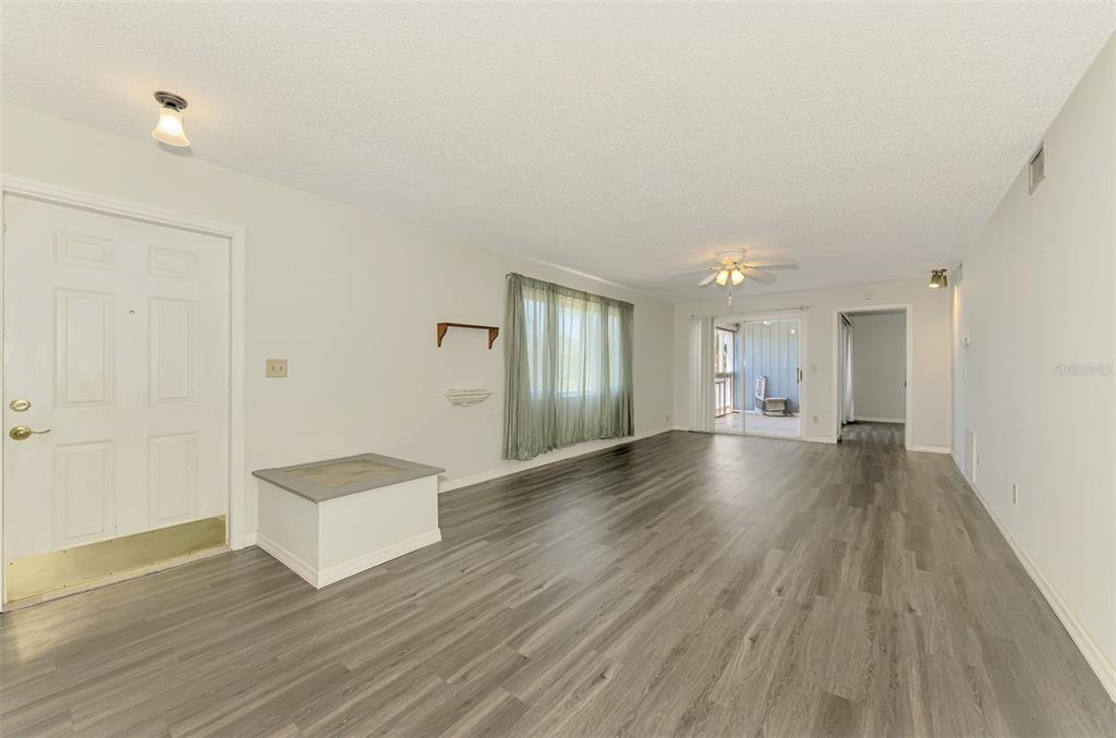 A living room with light walls, gray wood-look flooring, a ceiling fan, and sliding glass doors — 200 ROTONDA BOULEVARD W UNIT A2, ROTONDA WEST, FL