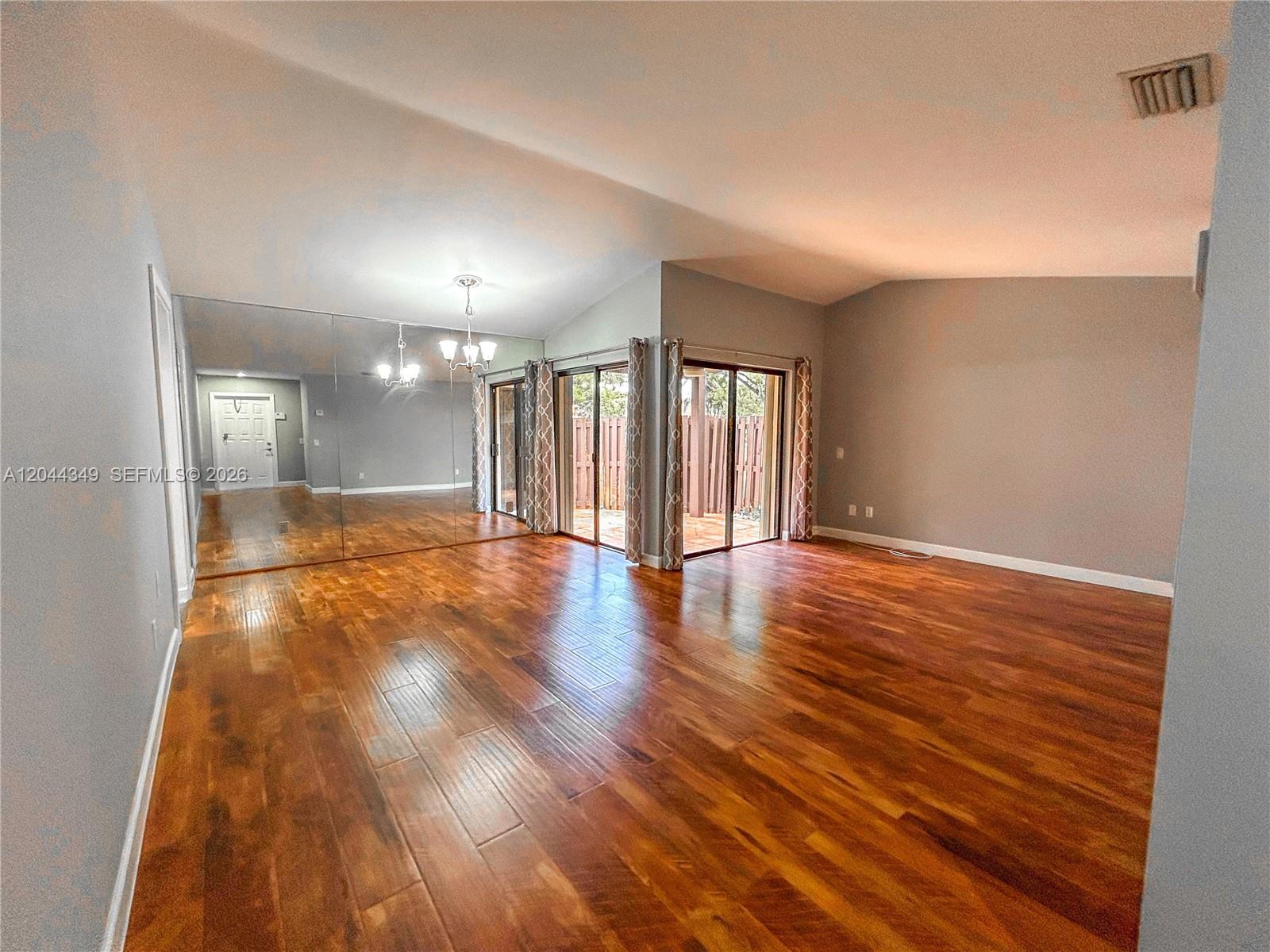 A spacious living room features hardwood floors, a mirrored wall, and sliding glass patio doors — 14970 SW 48th Ter # 27G, Miami FL 33185, MIAMI, FL
