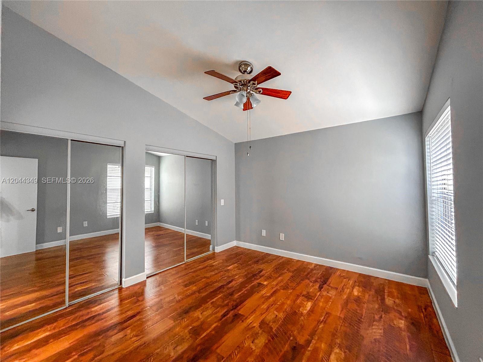 An empty bedroom features gray walls, hardwood floors, a ceiling fan, and mirrored closet doors — 14970 SW 48th Ter # 27G, Miami FL 33185, MIAMI, FL