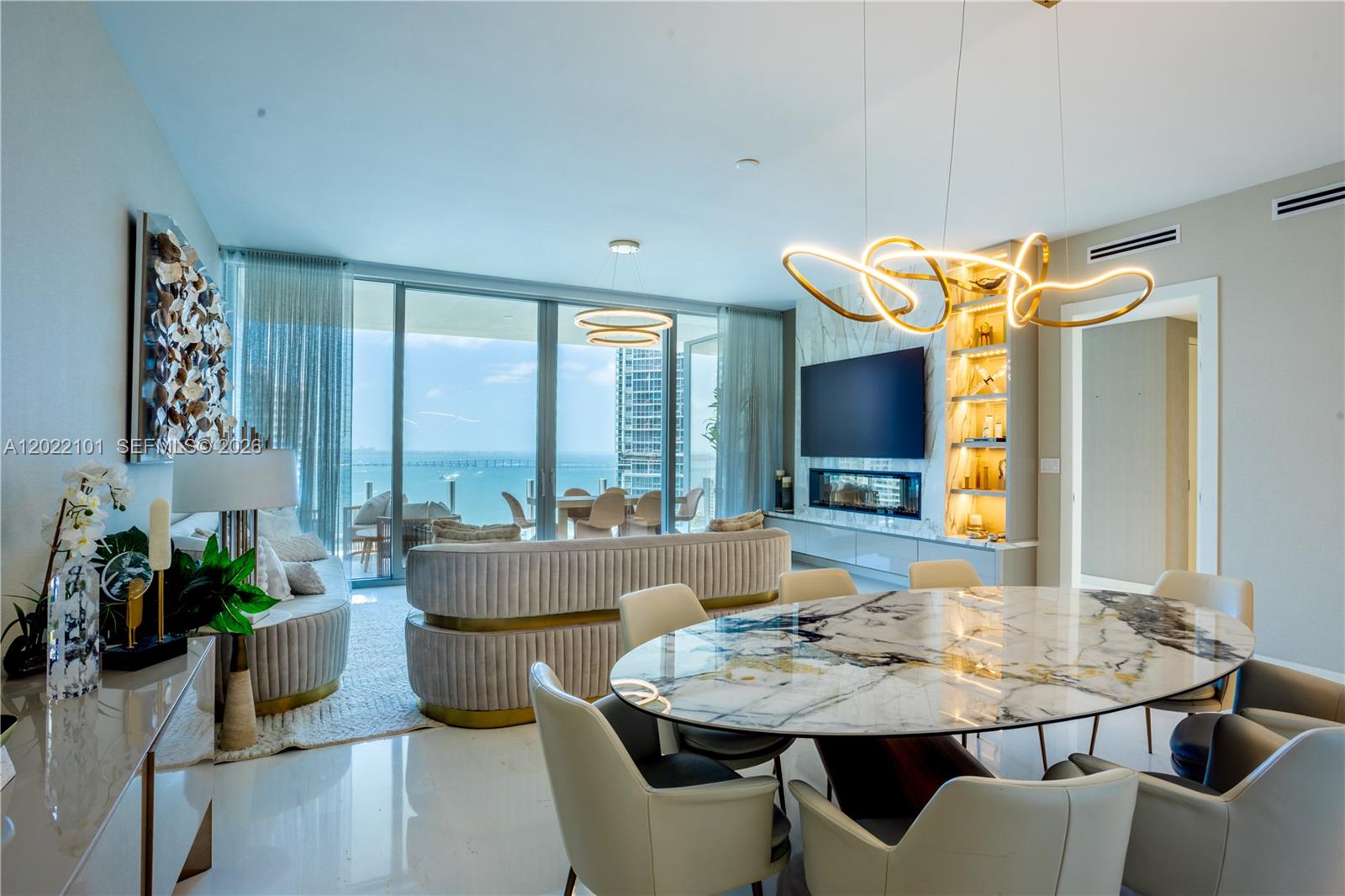 A modern living and dining room features a marble table, gold lighting, and ocean views — 300 Biscayne Boulevard Way # 2203C, Miami FL 33131, MIAMI, FL