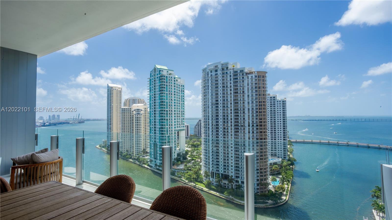A balcony with outdoor furniture overlooks a bay, high-rise buildings, and a bridge — 300 Biscayne Boulevard Way # 2203C, Miami FL 33131, MIAMI, FL
