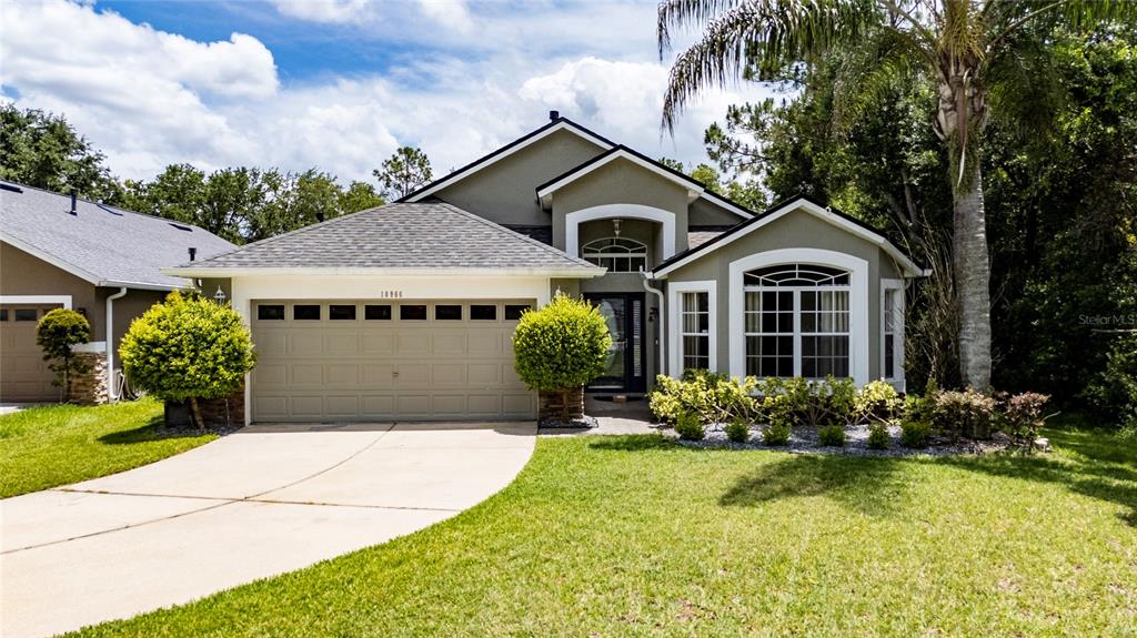 A single-story suburban house with a two-car garage, manicured shrubs, and a palm tree — 10966 ELIOTTI STREET, ORLANDO, FL