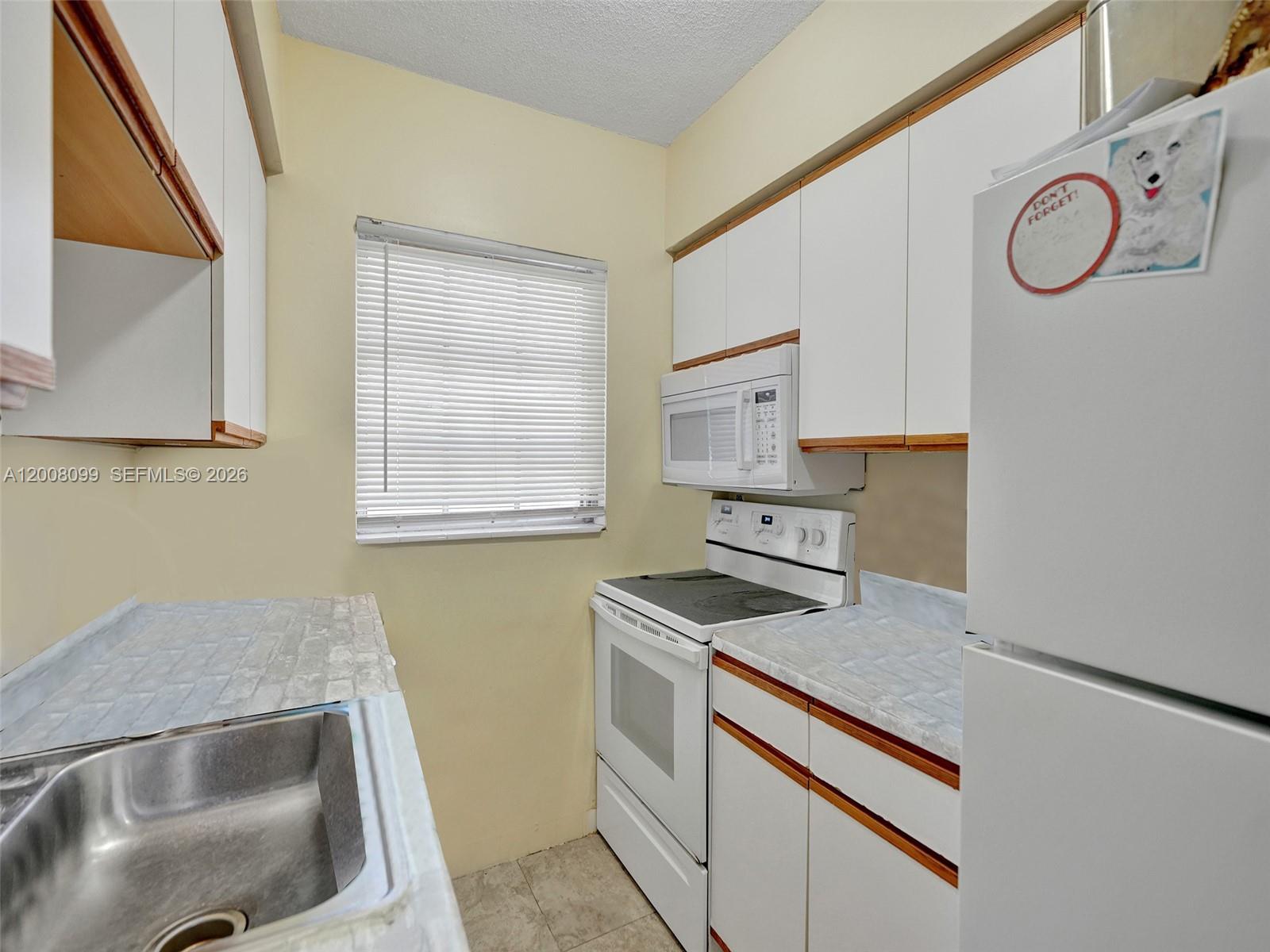 A small kitchen features white cabinets, a white stove, a microwave, and a sink — 1211 NE 23rd Ave # 2, Pompano Beach FL 33062, POMPANO BEACH, FL