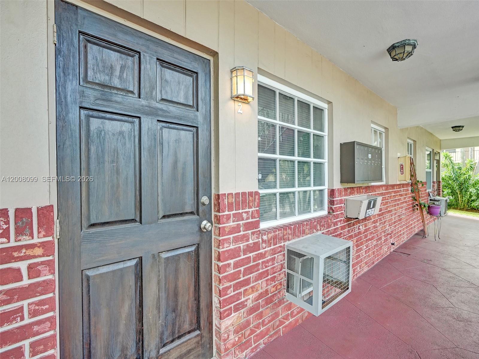 A dark wooden door and a window with a brick facade line an outdoor walkway — 1211 NE 23rd Ave # 2, Pompano Beach FL 33062, POMPANO BEACH, FL