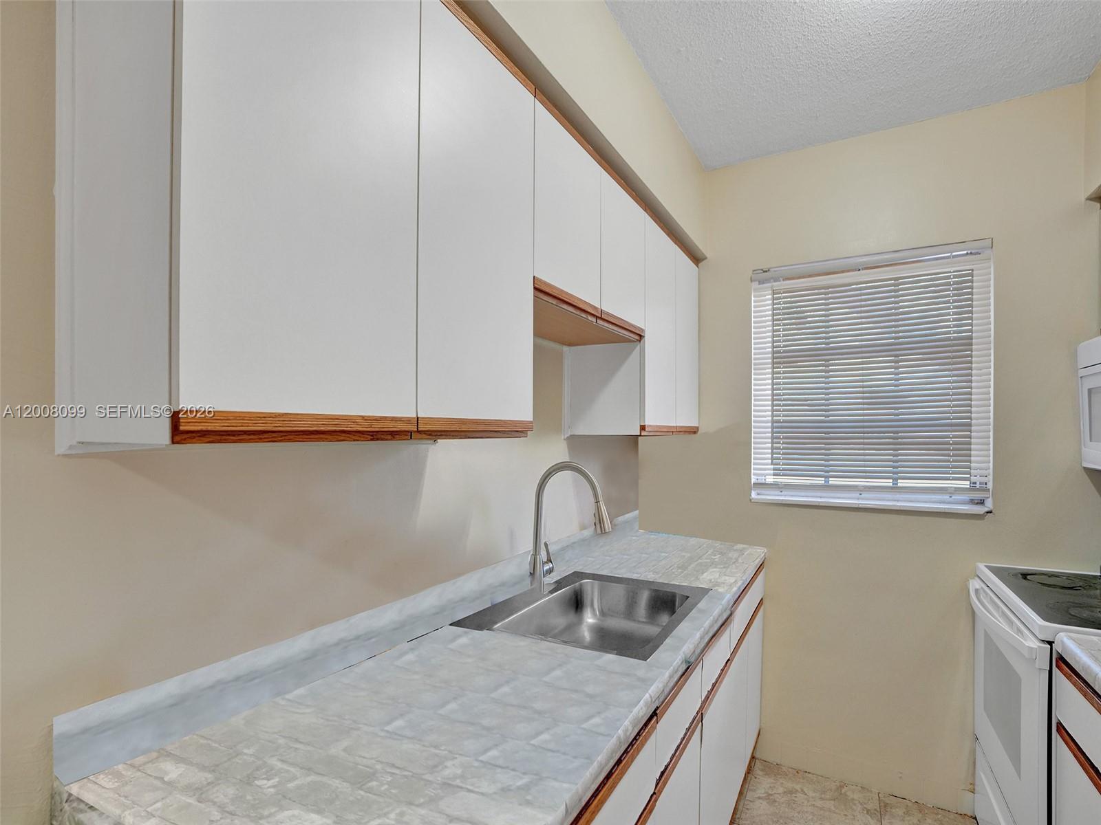 A kitchen features white cabinets, a stainless steel sink, and a marble-patterned laminate countertop — 1211 NE 23rd Ave # 2, Pompano Beach FL 33062, POMPANO BEACH, FL