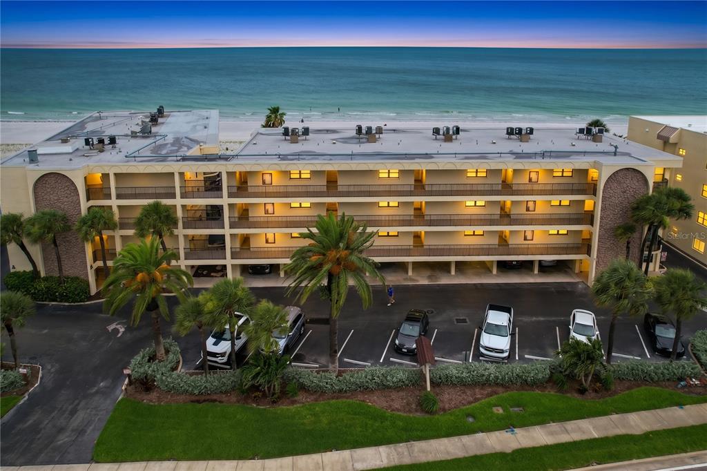 An aerial view shows a multi-story beachfront apartment building with a parking lot in front — 3500 GULF BOULEVARD UNIT 203, BELLEAIR BEACH, FL