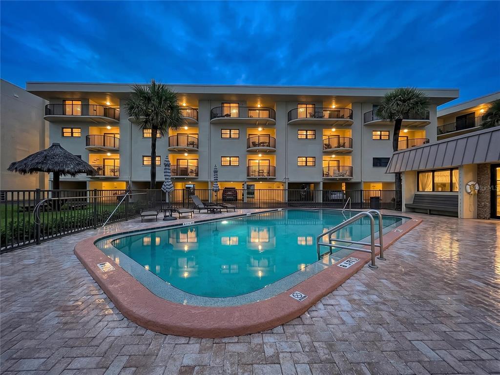 A swimming pool sits in front of a multi-story apartment building at dusk — 3500 GULF BOULEVARD UNIT 203, BELLEAIR BEACH, FL
