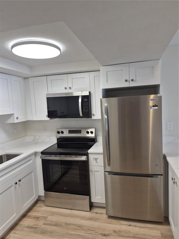 A kitchen features white cabinets, stainless steel appliances, and light wood-look flooring — 8151 BLIND PASS ROAD UNIT 6, ST PETE BEACH, FL