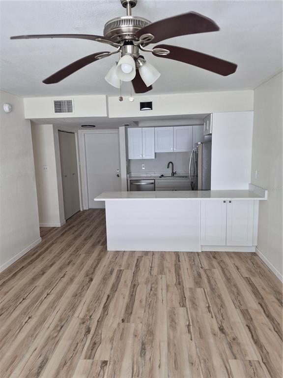 A kitchen with white cabinets and a breakfast bar overlooks a room with wood-look flooring — 8151 BLIND PASS ROAD UNIT 6, ST PETE BEACH, FL