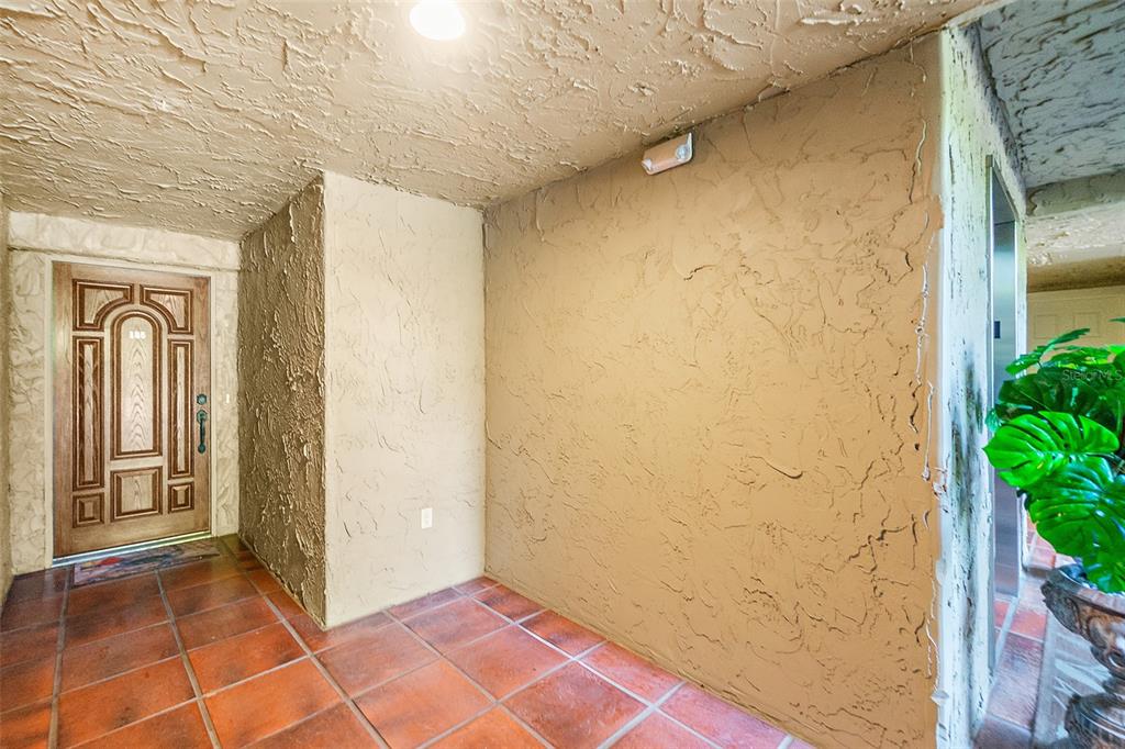 An entryway with a wooden door, textured walls, and terracotta tile flooring — 106 CLUB HOUSE DRIVE UNIT 106, PALM COAST, FL