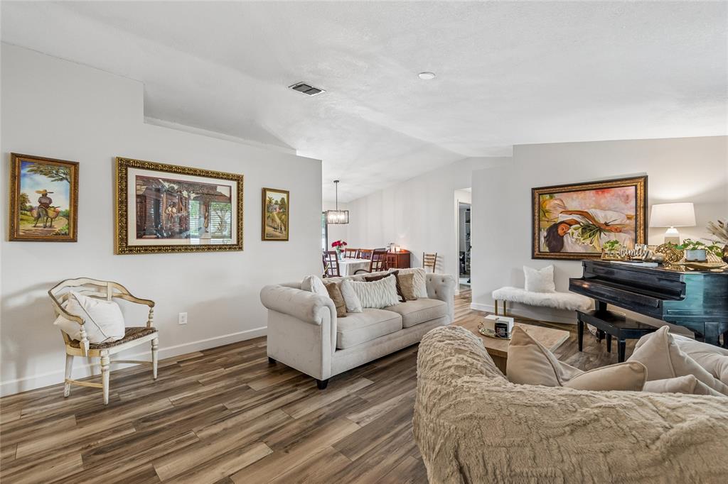 A living room features wood-look flooring, a sofa, a piano, and framed wall art — 15116 TRAIL CREEK PLACE, TAMPA, FL