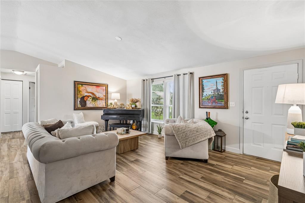 A living room features wood-look tile flooring, a tufted sofa, an armchair, and a piano — 15116 TRAIL CREEK PLACE, TAMPA, FL
