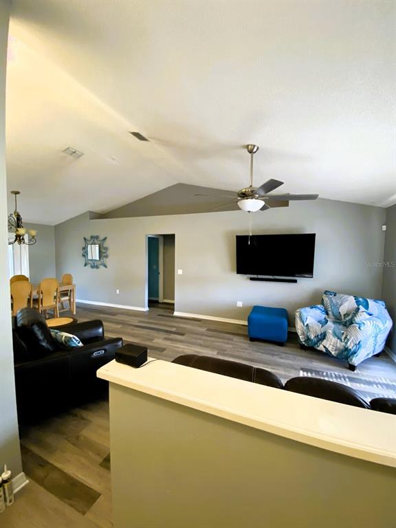 A living room with vaulted ceilings, wood-look flooring, a wall-mounted television, and a ceiling fan — 111 LINDALE STREET, LAKELAND, FL