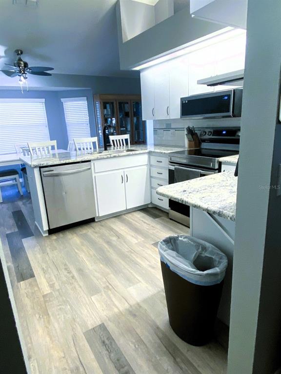 A kitchen features white cabinets, granite countertops, stainless steel appliances, and light wood-look flooring — 111 LINDALE STREET, LAKELAND, FL