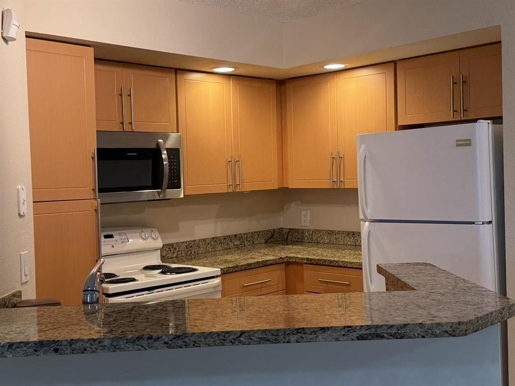A kitchen features light wood cabinets, granite countertops, and white appliances — 3390 Pinewalk Drive N # 1012, Margate FL 33063, MARGATE, FL