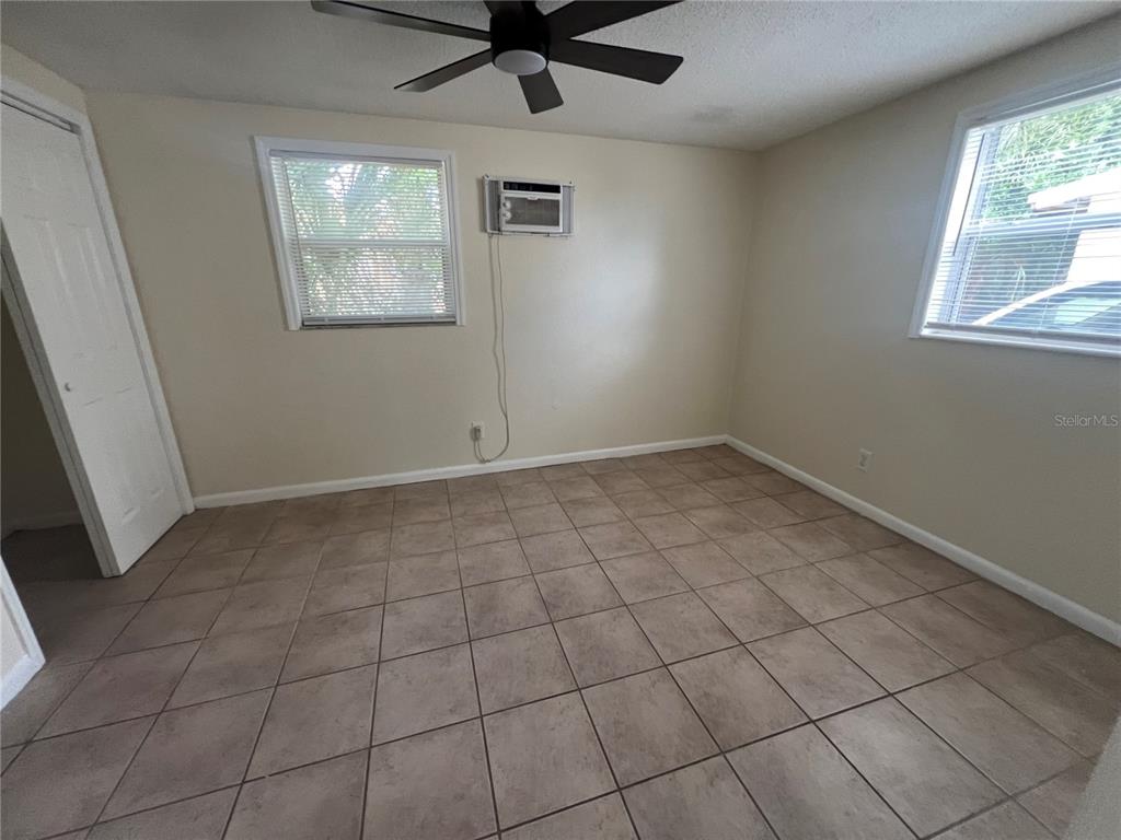 An empty room features beige tile flooring, two windows, a ceiling fan, and a wall-mounted AC — 275 PINEAPPLE STREET UNIT B, ENGLEWOOD, FL