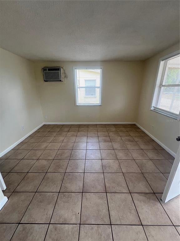 An empty room features beige tiled flooring, light-colored walls, two windows, and a wall-mounted air conditioner — 275 PINEAPPLE STREET UNIT B, ENGLEWOOD, FL