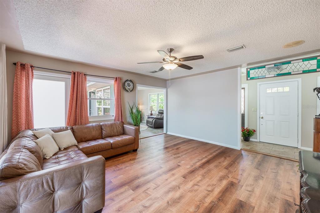 A living room with wood-look flooring, a brown leather sectional sofa, and a ceiling fan — 111 KIRBY TRAIL, MELROSE, FL