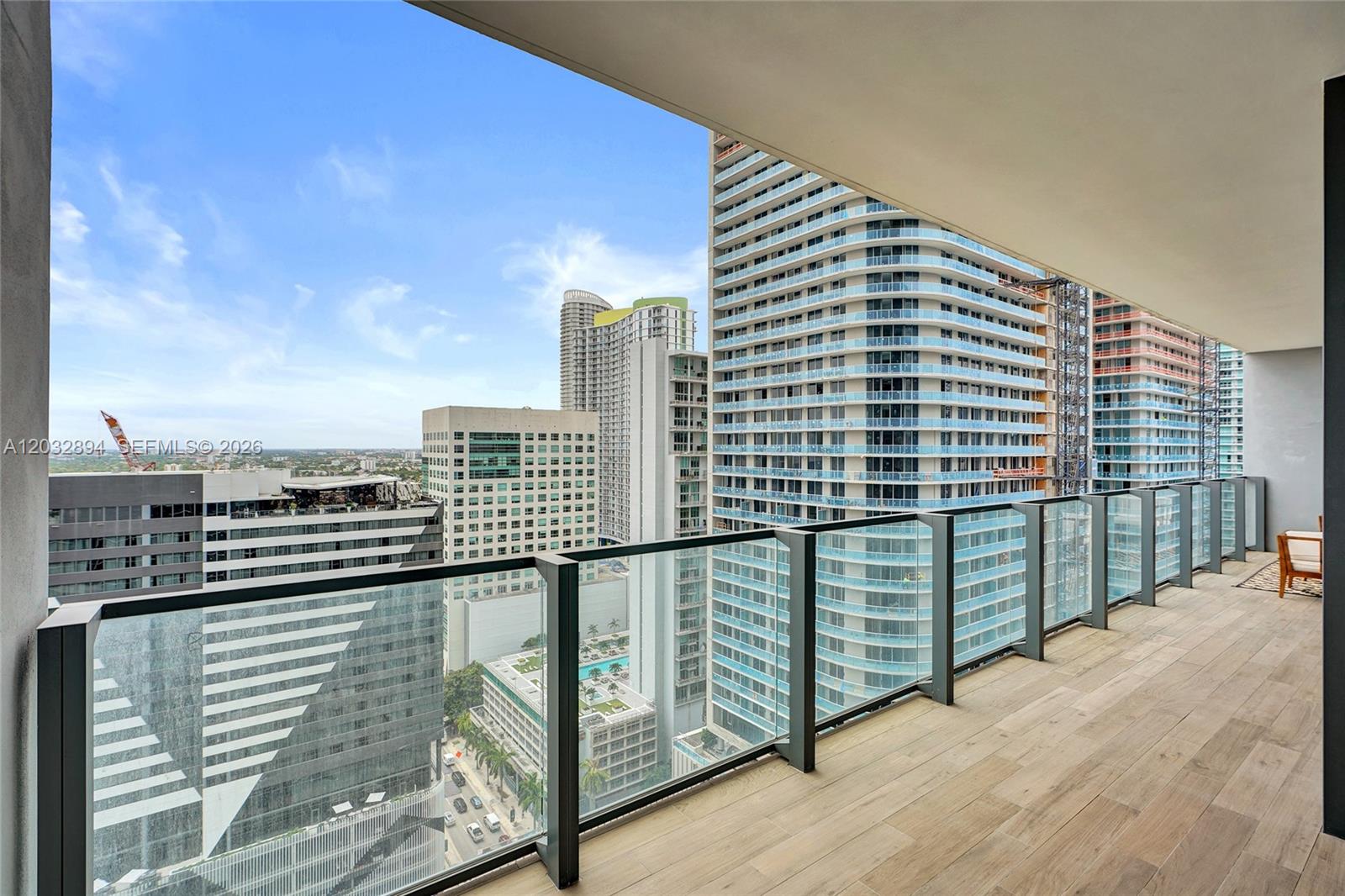A high-rise balcony features wood-look tile flooring, a glass railing, and views of surrounding skyscrapers — 88 SW 7th St # 2210, Miami FL 33130, MIAMI, FL