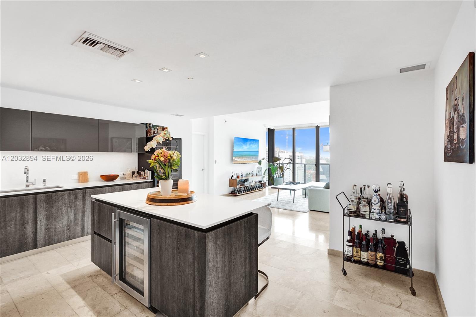 A modern kitchen with dark cabinetry and a white island opens into a bright living area — 88 SW 7th St # 2210, Miami FL 33130, MIAMI, FL