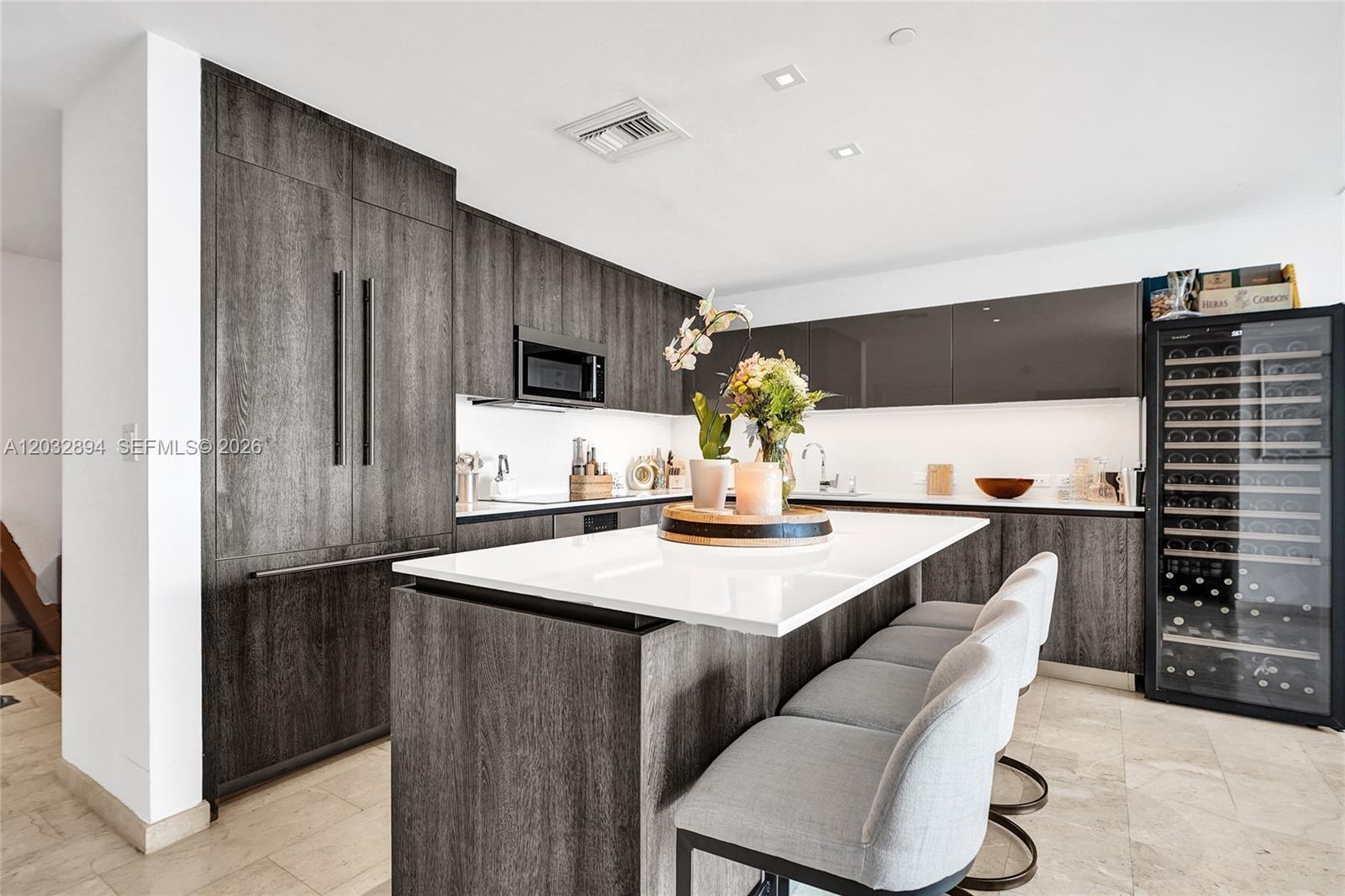 A modern kitchen features dark wood cabinetry, a white island, and a tall wine refrigerator — 88 SW 7th St # 2210, Miami FL 33130, MIAMI, FL