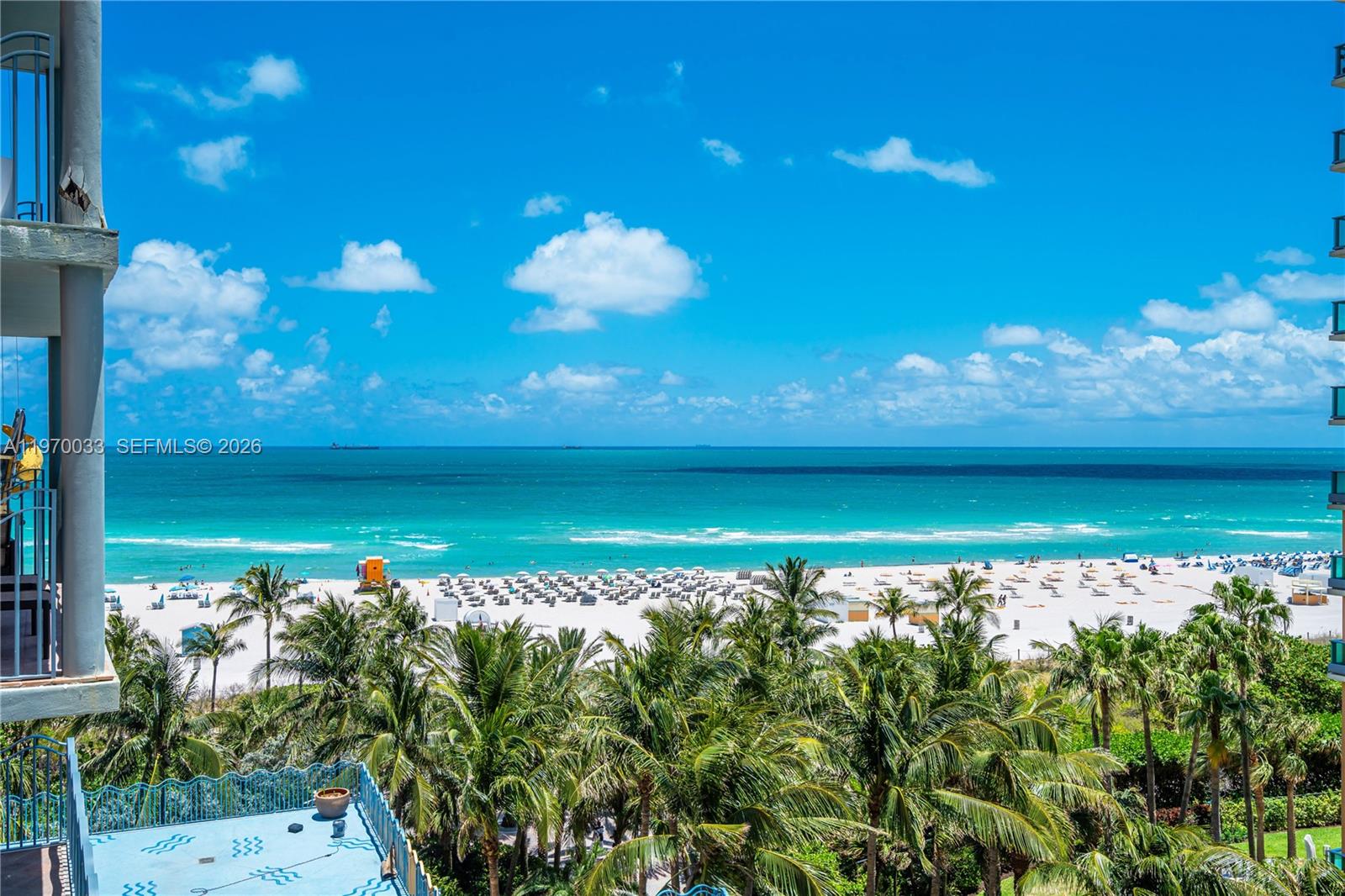 An elevated view of a sandy beach, ocean, and palm trees from a balcony — 1500 Ocean Dr # 704, Miami Beach FL 33139, MIAMI BEACH, FL