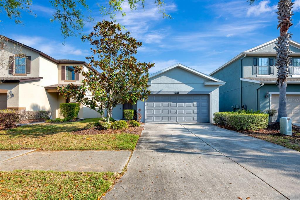 A light blue house with a two-car garage and a driveway sits between two neighbors — 9116 MOUNTAIN CAMELLIA LANE, RIVERVIEW, FL