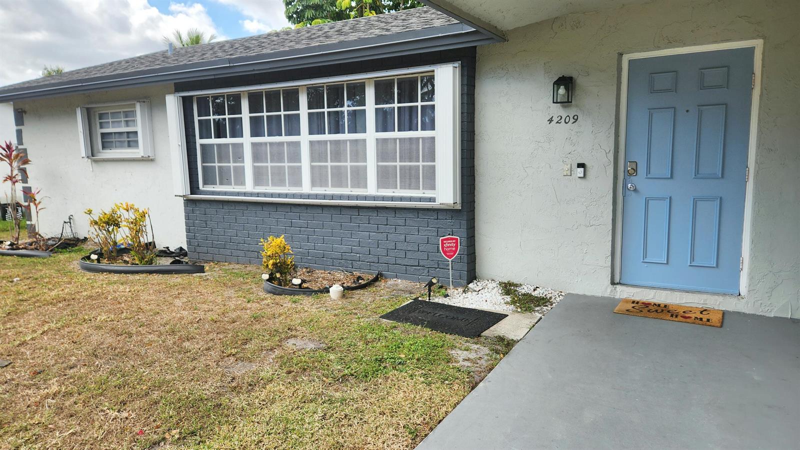 The exterior of a house features a blue front door, a large window, and landscaping — 4209 Waverly Drive, West Palm Beach FL 33407, WEST PALM BEACH, FL