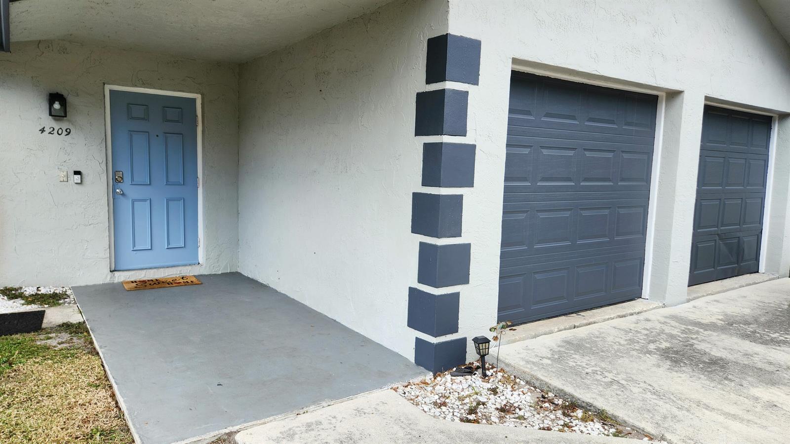 A light-colored house exterior features a blue front door and two dark gray garage doors — 4209 Waverly Drive, West Palm Beach FL 33407, WEST PALM BEACH, FL