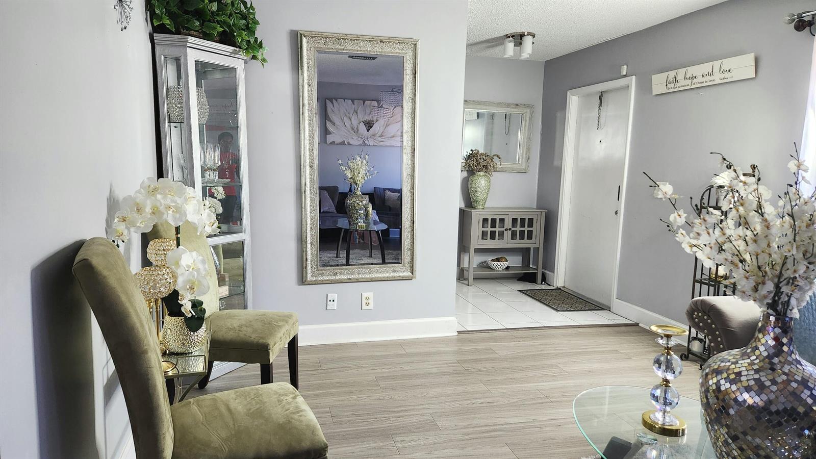 A living room with light wood floors, a large wall mirror, and two olive chairs — 4209 Waverly Drive, West Palm Beach FL 33407, WEST PALM BEACH, FL