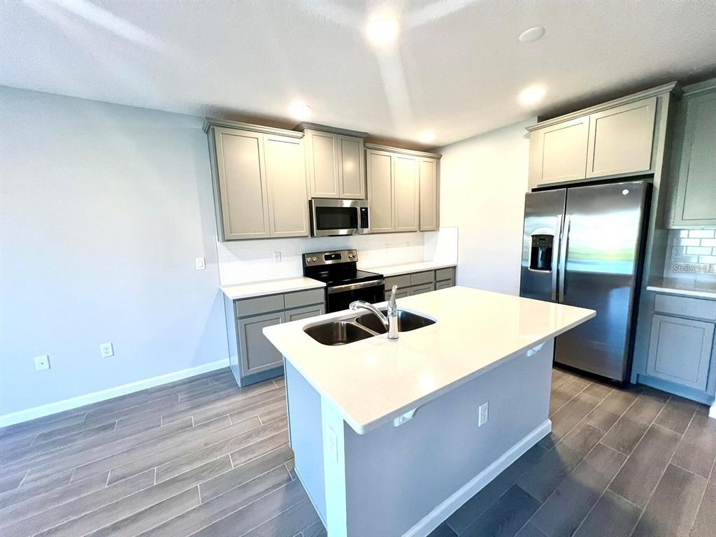 A kitchen features gray cabinets, stainless steel appliances, a central island, and wood-look tile flooring — 2774 NARCOOSSEE COMMONS WAY, ST CLOUD, FL