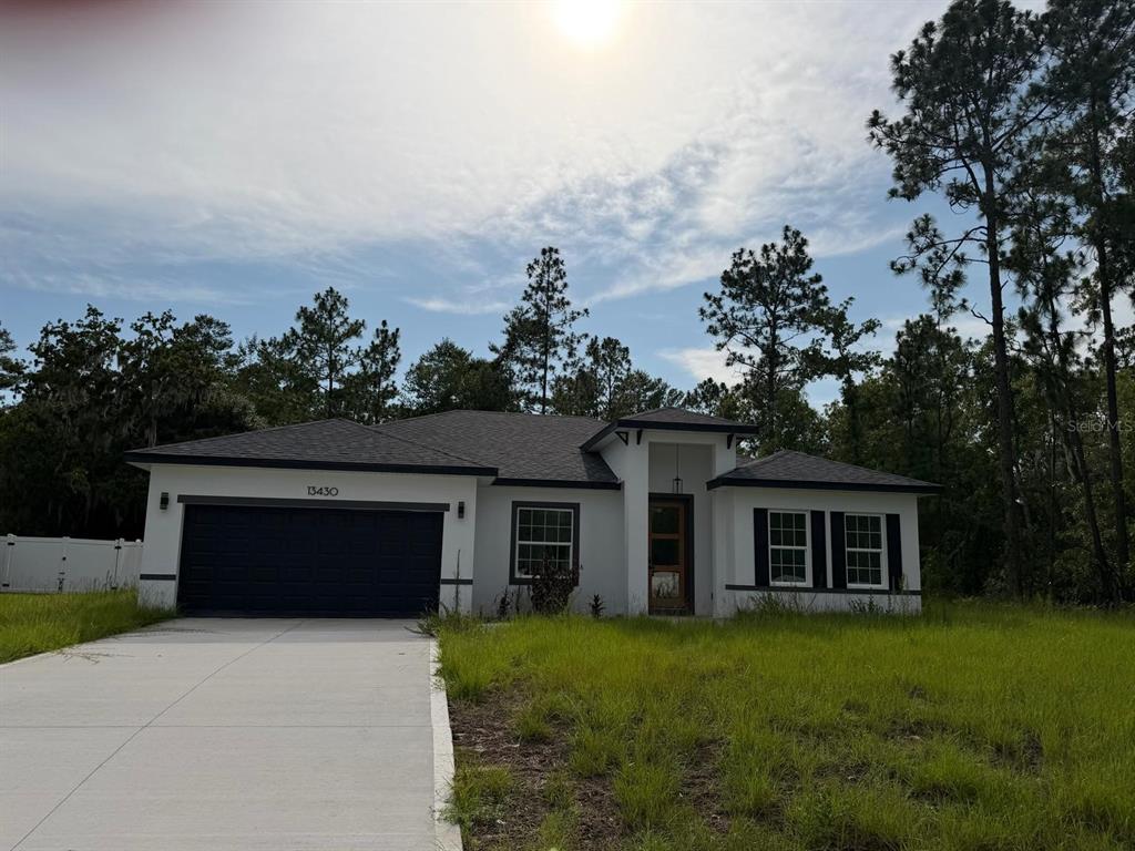A single-story house with a white stucco exterior, dark trim, and a two-car garage — 13430 SW 88TH TERRACE, DUNNELLON, FL