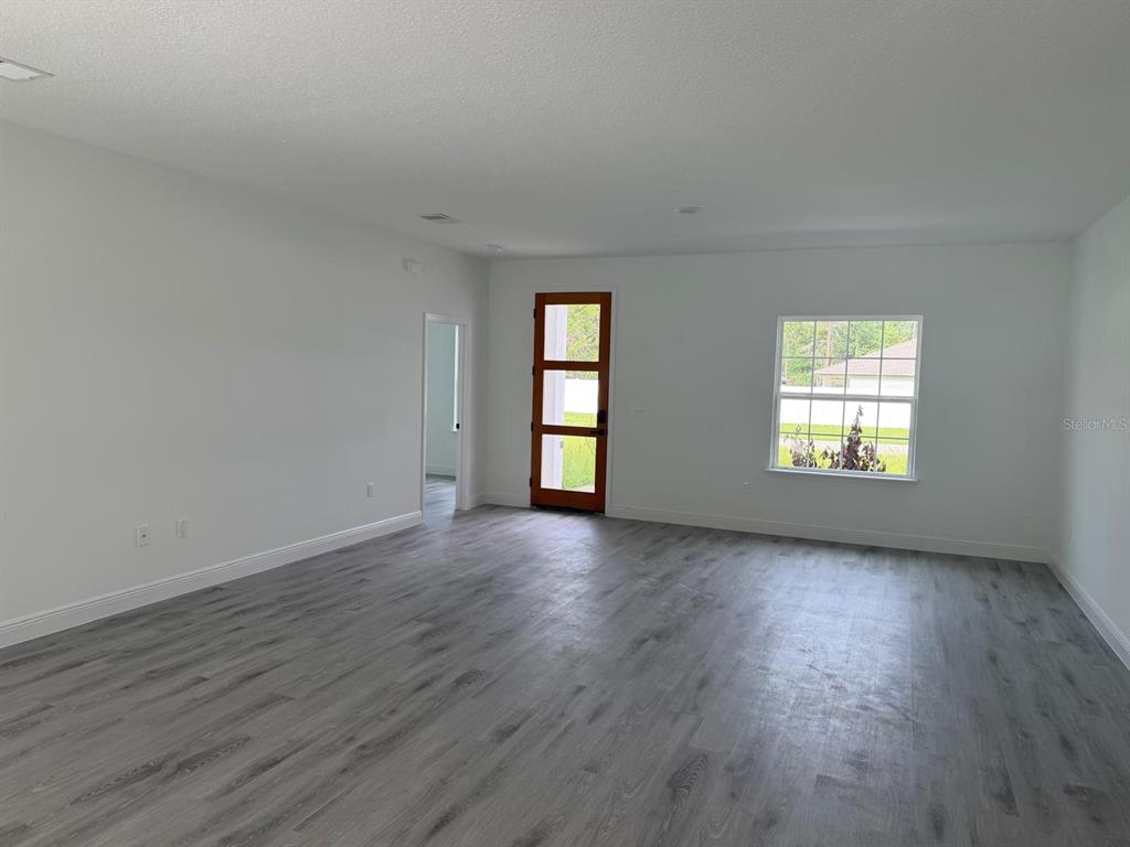 An empty room features gray wood-look flooring, white walls, a wooden front door, and windows — 13430 SW 88TH TERRACE, DUNNELLON, FL