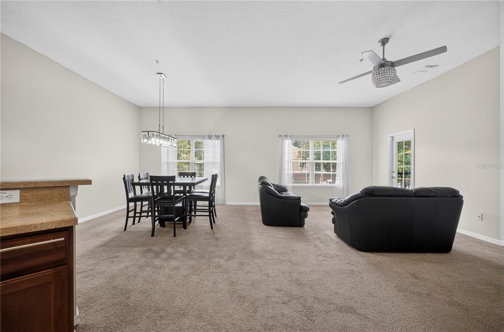 An open-concept living and dining area features beige carpeting, black leather furniture, and a ceiling fan — 380 ASHLEY BROOKE COURT UNIT C, APOPKA, FL