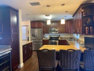 A kitchen features dark wood cabinets, stainless steel appliances, and a breakfast bar with wicker chairs — 20020 NE 6th Court, Miami FL 33179, MIAMI, FL