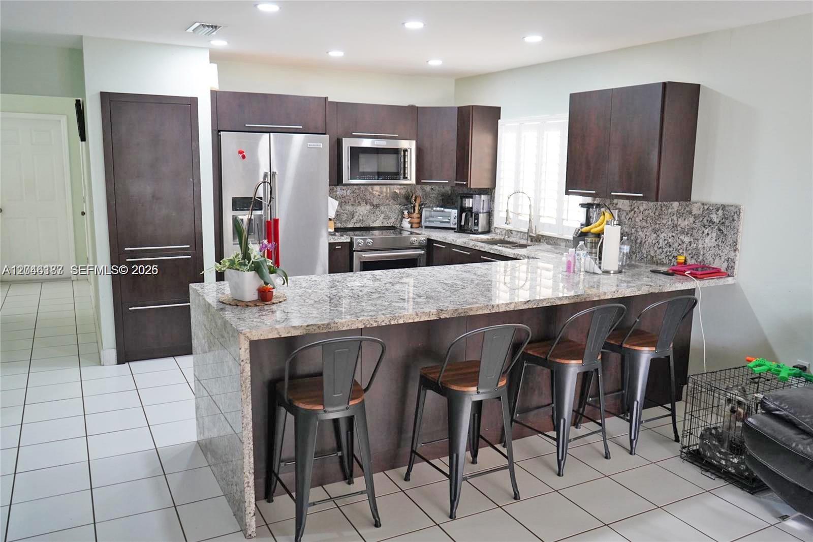 A kitchen features dark wood cabinets, granite countertops, and four metal bar stools — 3461 SW 154th Ct, Miami FL 33185, MIAMI, FL