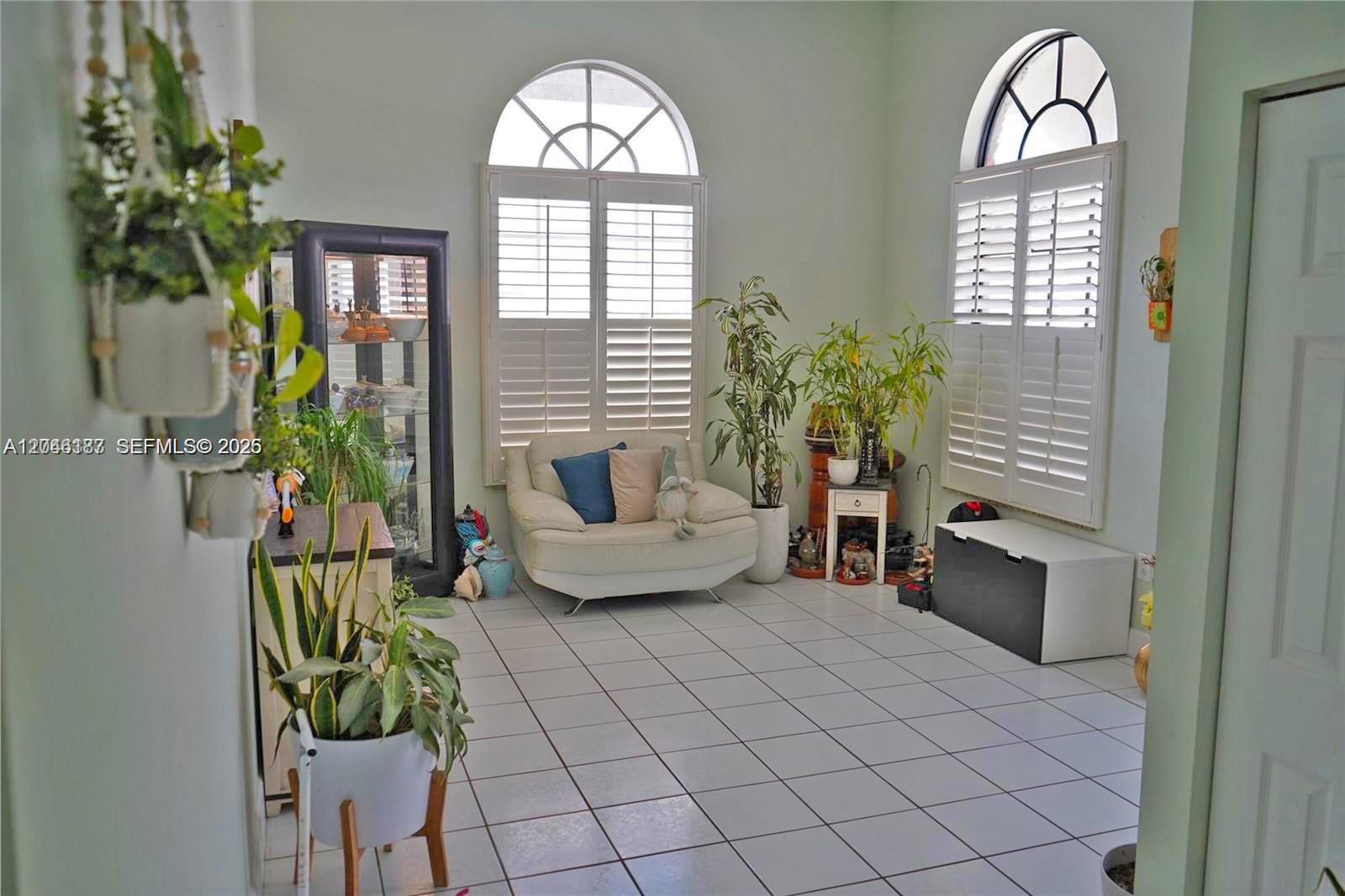 A sunlit room features white tile floors, two arched windows with shutters, and several potted plants — 3461 SW 154th Ct, Miami FL 33185, MIAMI, FL