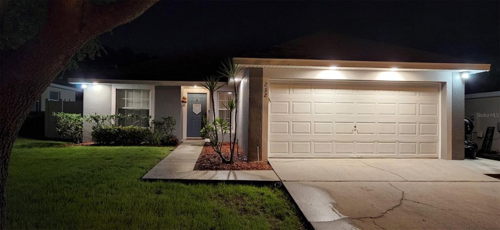 A single-story house with a white garage door and a blue front door at night — 232 CRESTWOOD PASS, DAVENPORT, FL