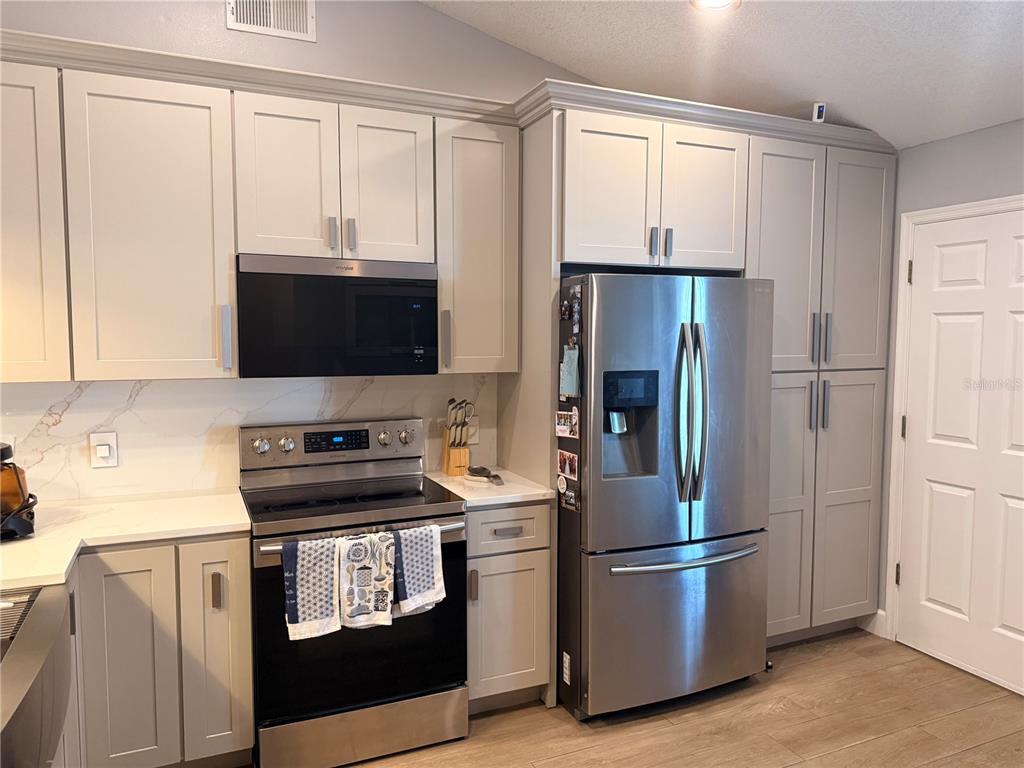 A kitchen features light gray cabinetry, stainless steel appliances, and a white marble-look backsplash — 232 CRESTWOOD PASS, DAVENPORT, FL