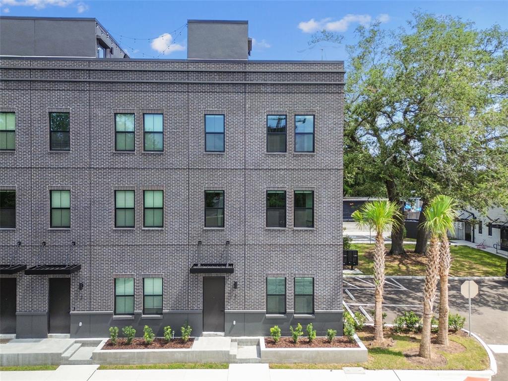 A three-story gray brick townhouse features dark window frames and a small landscaped front yard — 1218 E KAY STREET UNIT 27, TAMPA, FL