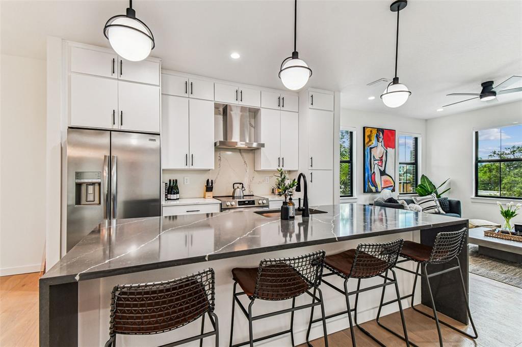 A modern kitchen features white cabinetry, a dark stone island, and three bar stools — 1218 E KAY STREET UNIT 27, TAMPA, FL