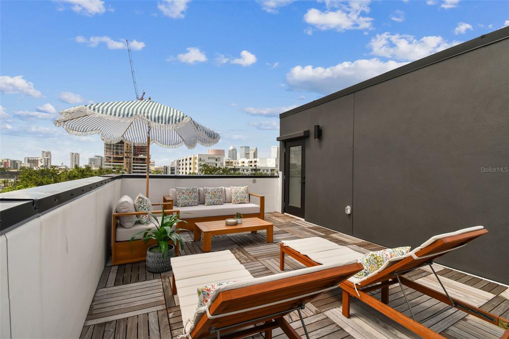 A rooftop terrace features wooden decking, outdoor lounge furniture, a striped umbrella, and city views — 1218 E KAY STREET UNIT 27, TAMPA, FL