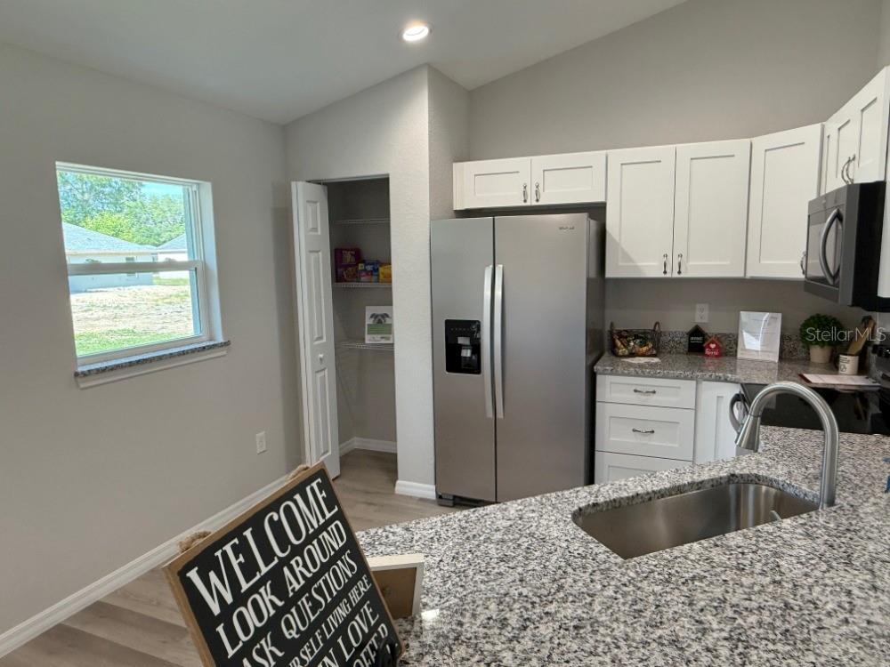 A kitchen features white cabinets, granite countertops, a stainless steel refrigerator, and a walk-in pantry — 13337 SW 112 STREET, DUNNELLON, FL