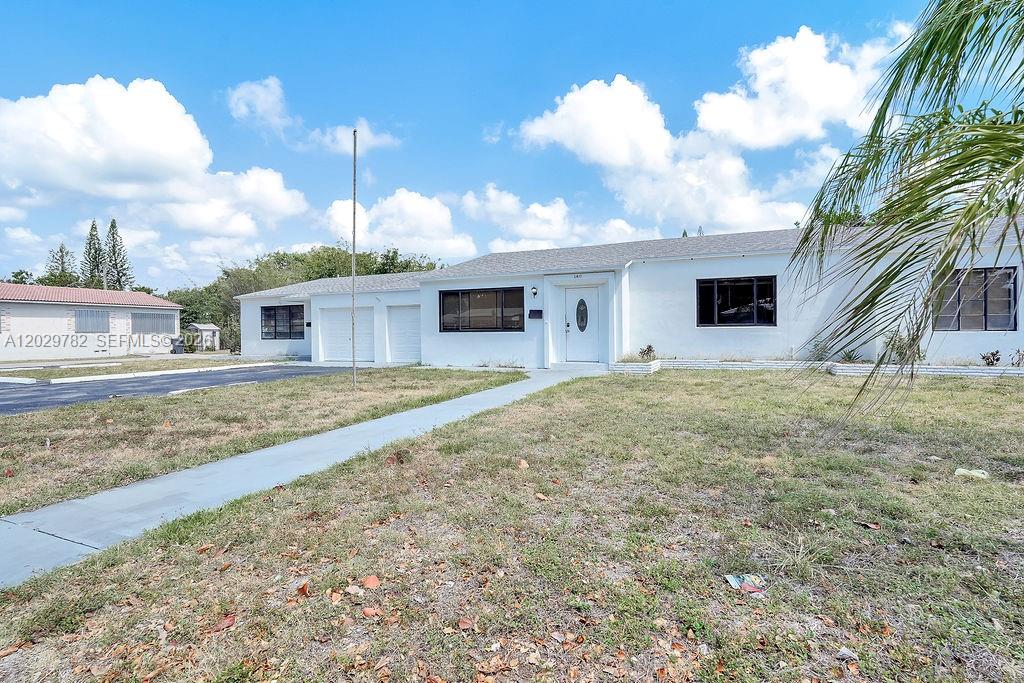 A white single-story house with a flat roof and a paved driveway under a cloudy sky — 2417 Pierce St, Hollywood FL 33020, HOLLYWOOD, FL