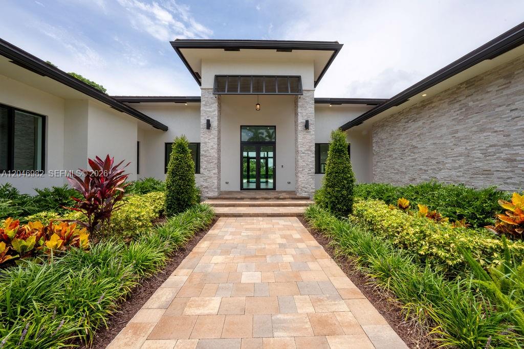 A stone-accented entryway leads to a modern home with a paved walkway and landscaping — 11861 NW 9th St, Plantation FL 33325, PLANTATION, FL