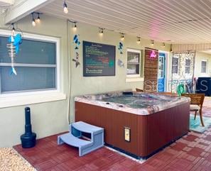 A hot tub sits on a brick patio under a covered porch with string lights — 604 7TH AVENUE SW, LARGO, FL