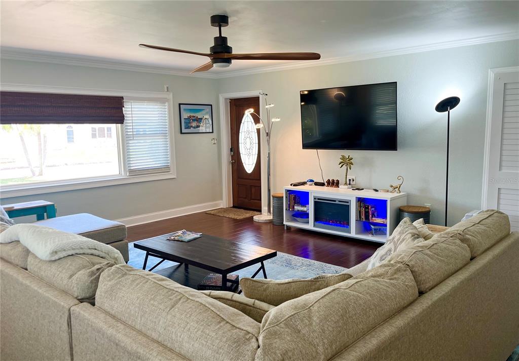 A living room features a sectional sofa, a television above a fireplace console, and hardwood floors — 604 7TH AVENUE SW, LARGO, FL
