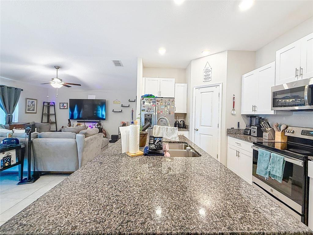 A kitchen with granite countertops and white cabinets overlooks an open-concept living room — 13360 WILLOW BLUESTAR LOOP, RIVERVIEW, FL