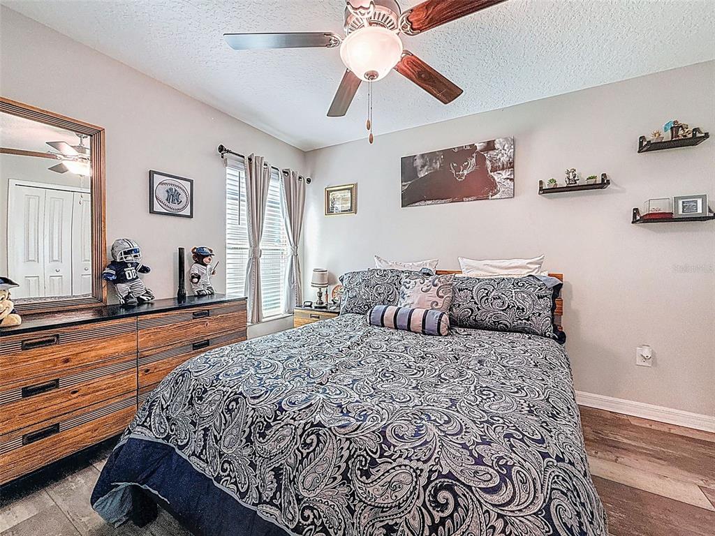 A bedroom features a bed with a paisley comforter, a wooden dresser, and ceiling fan — 13360 WILLOW BLUESTAR LOOP, RIVERVIEW, FL